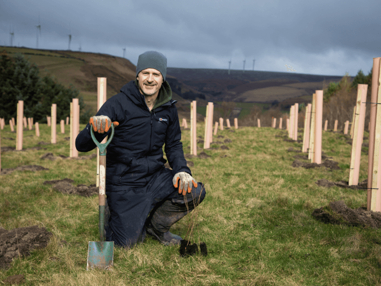 Man smiling with spade whilst carrying out tree planting at site