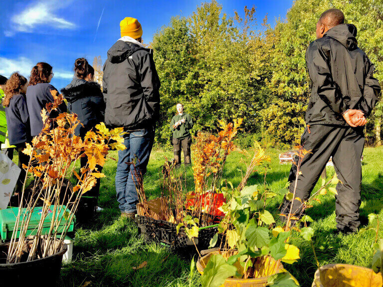 Volunteers listening to tree planting demo surrounded by whips