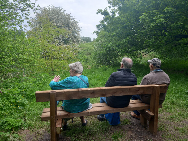three older people enjoying view of a woodland from a bench in Sale