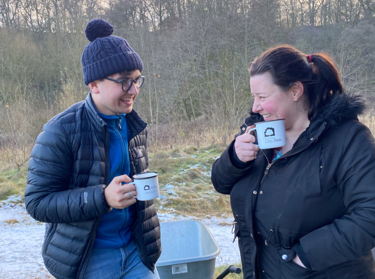 Two volunteers laughing with city of trees mugs