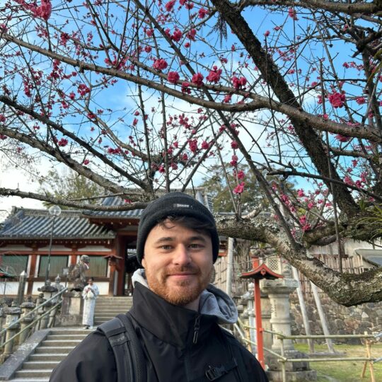 Man in front of a blossom tree smiling with hat on